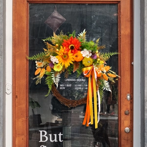 Autumn door wreath with sunflowers, pumpkins, and long tassels on a rustic glass door