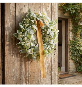Detail of faux gray leaves and white daisy wreath with mustard velvet ribbon on old wooden door