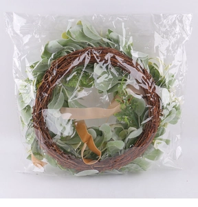 Close-up of decorative artificial eucalyptus wreath with brown rattan base on white surface