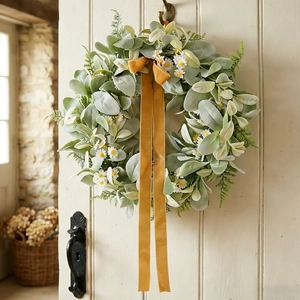 Artificial wreath with grey leaves and white flowers on a door with a yellow velvet ribbon
