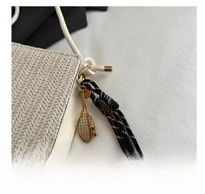 Detail of woven beige bag featuring a gold tennis racket charm and tricolor braided cord