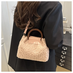 Detail der Teddy-Plüschtasche mit Holzgriff und Lederriemen vor schwarzem Blazer