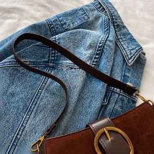Close-up of brown suede handbag with golden circular buckle and leather shoulder strap