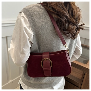 Detail of burgundy suede shoulder bag with gold metal buckle on a model's arm