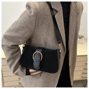 Détail d'un sac sous le bras noir vintage avec boucle fer à cheval dorée sur blazer
