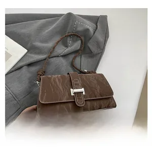 Gros plan du sac à bandoulière marron plissé avec boucle en argent sur une veste grise