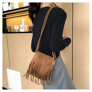 Brown fringe crossbody bucket bag in matte suede texture shown on model in a cozy cafe