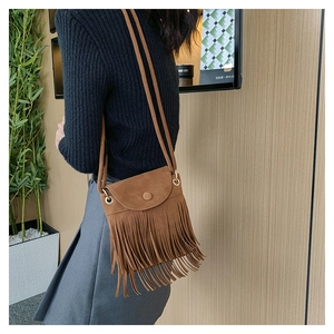 Close-up of a brown matte tassel bucket bag with gold hardware worn as a crossbody