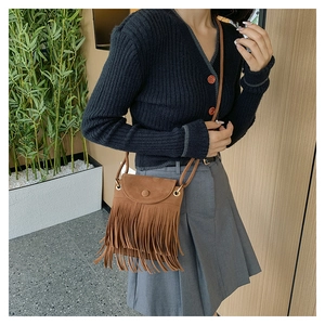 Close-up of a brown suede tassel bucket bag shown on a model with a cross-body strap