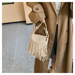 Detail of a beige matte bucket bag with long fringe and knotted handle on a trench coat