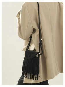 Detail of a black tassel bucket bag with matte suede texture and gold hardware on model