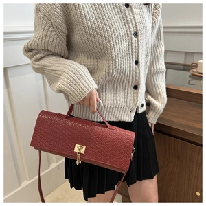 Detailed view of woven burgundy shoulder bag with gold square clasp and pendant accent