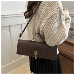 Detail of dark brown woven texture shoulder bag with golden twist lock on white sweater