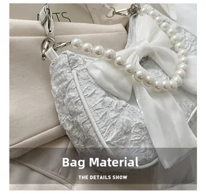 Macro detail of white pleated bag featuring elegant pearl handle and organza bow
