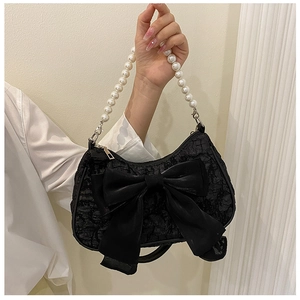 Detail of black pleated handbag featuring large bow and white pearl handle strap