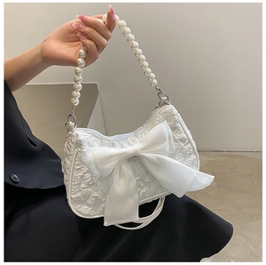 Detail of white pleated handbag with large organza bow and elegant pearl handle strap