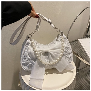 Detail of white pleated handbag featuring a large chiffon bow and pearl handle strap