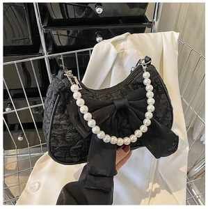 Detail of black pleated handbag featuring a large satin bow and white pearl handle strap