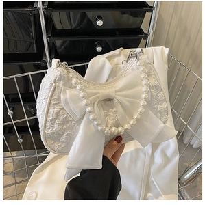 Close-up of white crescent bag with textured fabric, oversized bow and pearl chain handle