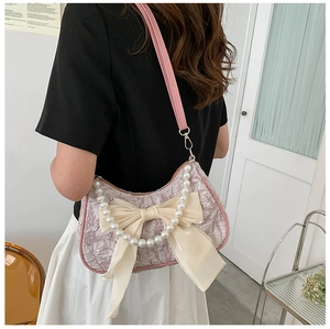 Detail of pink pleated handbag featuring a large cream bow and decorative pearl handle