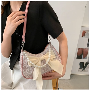 Detail of pink pleated crossbody bag featuring a large cream bow and pearl handle chain