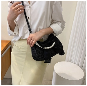 Detail of black pleated crossbody bag with velvet bow and pearl handle on a model