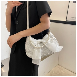 Detail of white pleated handbag with large bow and pearl handle on a female model