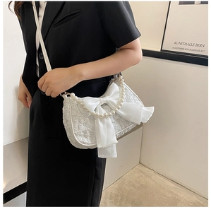 Detail of white textured shoulder bag featuring large bow and pearl strap accents