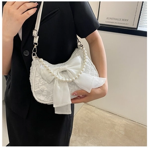 Detailed view of white pleated handbag with mesh bow and decorative pearl handle accents