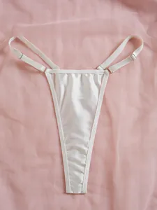 Détail d'un string en dentelle satinée blanche avec bretelles réglables sur fond rose