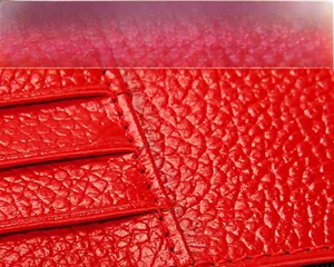 Détail macro de la texture du cuir litchi rouge et des coutures fines du porte-passeport