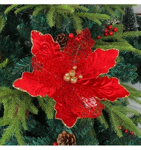 Détail d'un poinsettia de Noël rouge avec bords pailletés dorés sur une branche de sapin