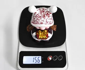 Close-up of a resin Christmas dwarf figurine being weighed on a scale showing 156 grams