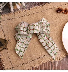 Close-up of burlap Christmas bow with pine and berry print on rustic jute background