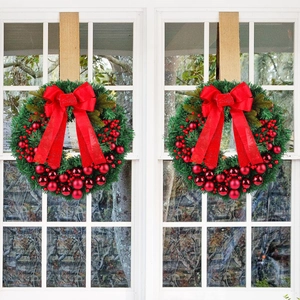 Set of two Christmas wreaths with red ornaments and bows on a white window frame