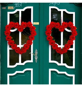 Detail of red rose heart wreaths hung on dark green wooden doors for Valentine's decor