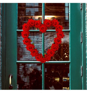 Detailed view of red heart-shaped rose wreath hanging on a green wooden door for Valentine decoration