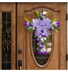 Detail van tulp kruis krans met paarse strik hangend aan een bruine houten deur
