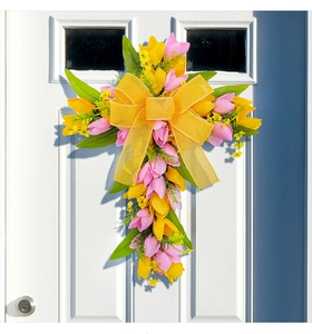 Detail van paaskrans in kruisvorm met tulpen en grote gele strik op een witte deur