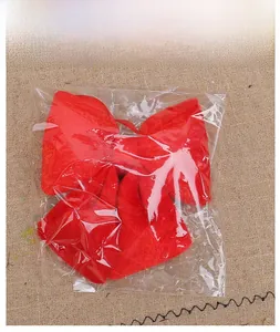 Detail view of large red velvet bow ornament in clear packaging on rustic background