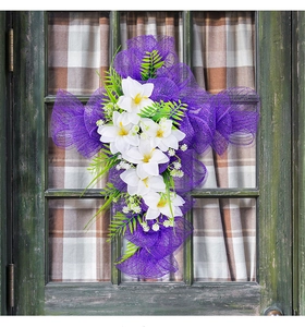 Dettaglio di ghirlanda a croce in rete viola con gigli bianchi su porta in legno verde