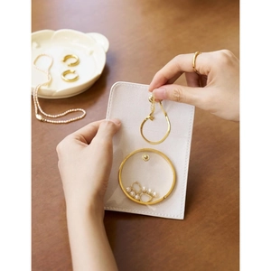 Close-up of cream jewelry organizer pouch showing gold necklaces and pearl earrings