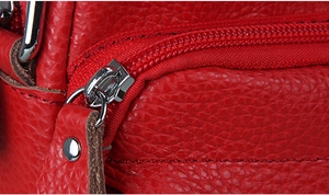 Macro detail of red pebbled leather bag featuring a silver metal zipper and hardware