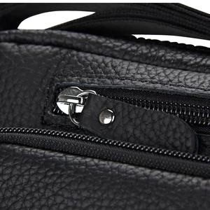 Detail view of silver metal zipper and black lychee grain leather texture on a shoulder bag