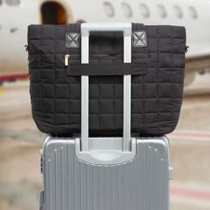 Black quilted tote bag with trolley sleeve and gold hardware for travel convenience