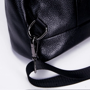 Detailed macro view of black pebbled leather texture and gunmetal buckle on the backpack