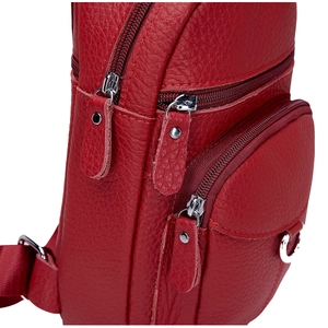 Detalle de bandolera de piel roja granulada con compartimentos con cremallera y remaches