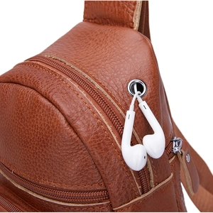Detalle de riñonera de cuero marrón con cremalleras múltiples y orificio para auriculares
