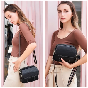 Detail of black lychee leather crossbody bag with decorative stitching and woven strap