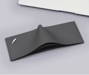 Detail of minimalist black leather wallet featuring tricolor metal tag on a gray desk